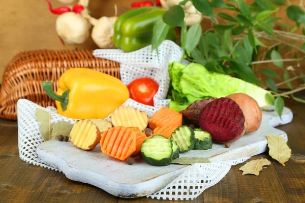 Beautiful sliced vegetables, on wooden board, on wooden background — Stock Photo, Image