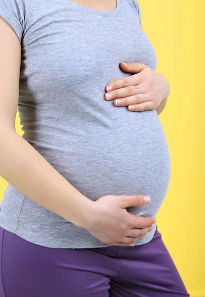 Pregnant woman touching her belly on yellow background — Stock Photo, Image