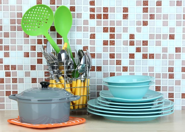 Dishes and cutlery in kitchen on table on mosaic tiles background — Stock Photo, Image