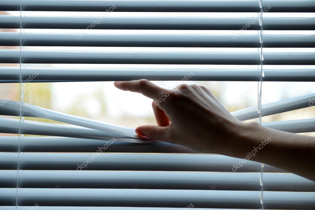 Female hand separating slats of venetian blinds with a finger to see through
