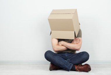 Adam başını duvara yakın katta oturan karton kutu