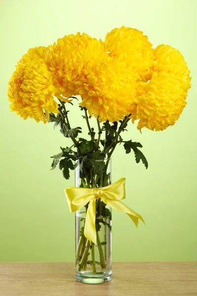 Zářivě žluté chryzantémy v skleněné vázy, na zeleném pozadí — Stock fotografie