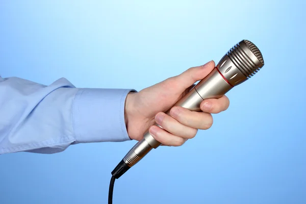 Männliche Hand mit Mikrofon auf blauem Hintergrund — Stockfoto