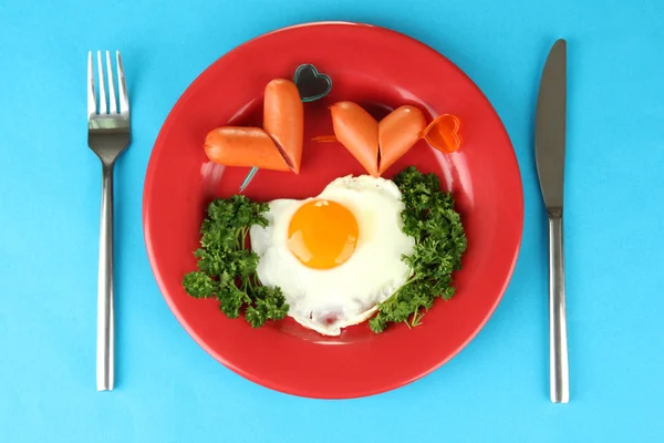 Salsicce sotto forma di cuori, uova strapazzate e prezzemolo, sul piatto di colore, sullo sfondo di colore — Foto Stock