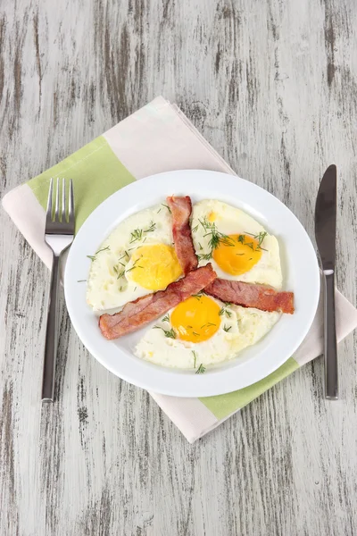 Ovos mexidos e bacon na placa no guardanapo na mesa de madeira — Fotografia de Stock