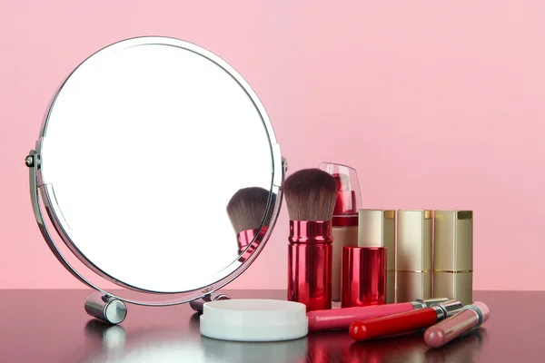 Espelho de mesa redonda com cosméticos na mesa no fundo rosa — Fotografia de Stock