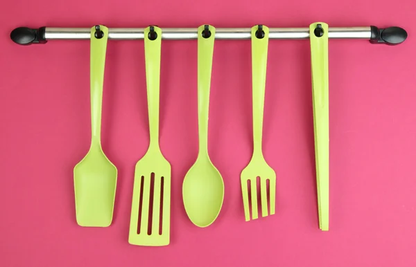 Plastic kitchen utensils on silver hooks on red background — Stock Photo, Image