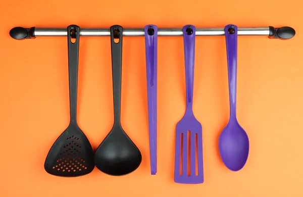 Plastic kitchen utensils on silver hooks on orange background — Stock Photo, Image