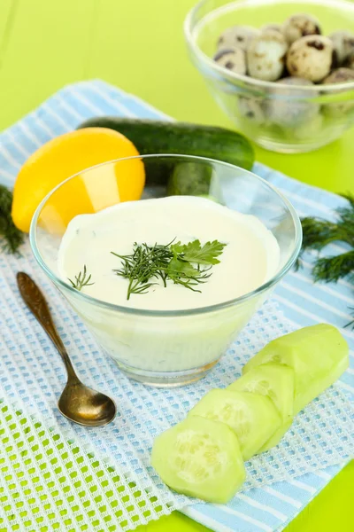 Komkommer yoghurt in glazen kom, op kleur servet, op houten achtergrond — Stockfoto