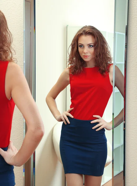 Bella ragazza cercando vestito vicino specchio in camera — Foto Stock