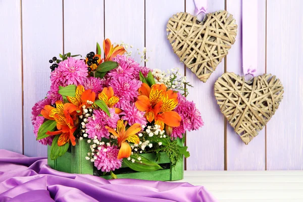 Flowers composition in crate with decorative hearts on table on wooden background — Stock Photo, Image