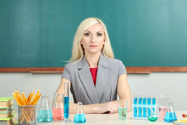 Chemielehrer sitzt am Tisch auf Tafel-Hintergrund — Stockfoto