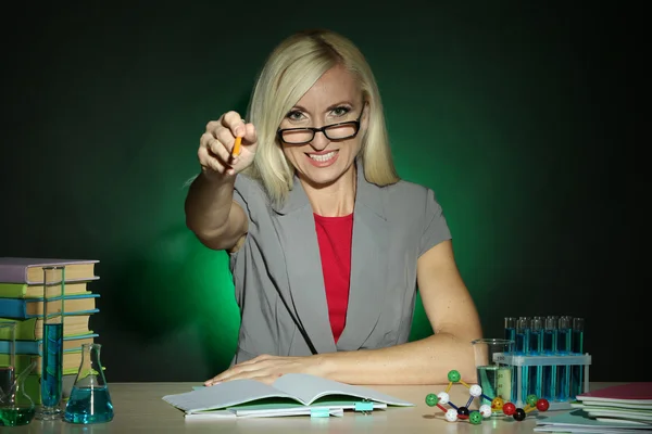 Koyu renkli arka plan üzerinde masada oturan wicked kimya öğretmeni — Stok fotoğraf