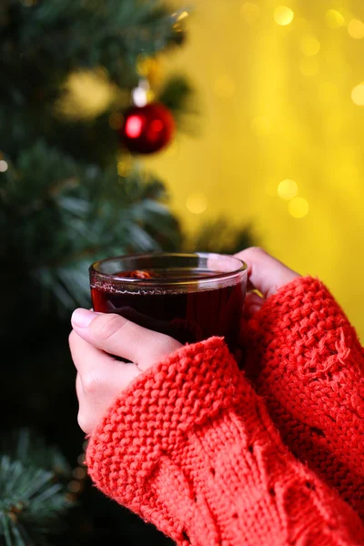 Hände halten Becher mit Heißgetränk, Nahaufnahme, auf dem Hintergrund des Weihnachtsbaums — Stockfoto
