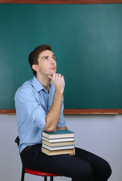 Νεαρός δάσκαλος κάθεται κοντά chalkboard σε σχολική τάξη — Φωτογραφία Αρχείου