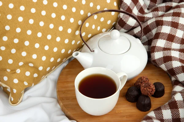 Tasse und Teekanne mit Bonbons auf Holzständer auf dem Bett aus nächster Nähe — Stockfoto