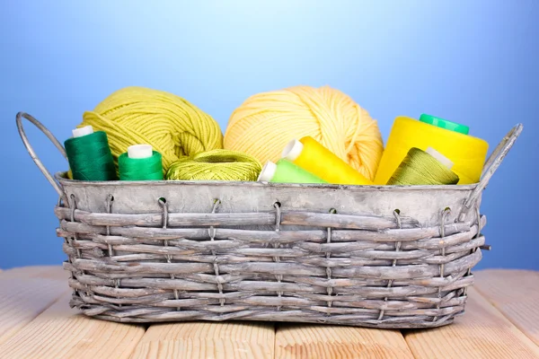 Bright threads in basket on wooden table on blue background — Stock Photo, Image