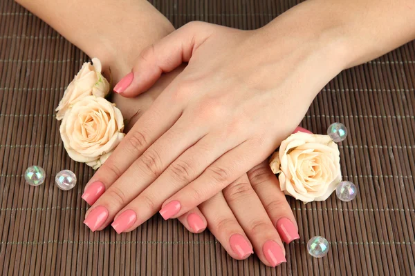 Mãos de mulher com manicure rosa e flores, em fundo tapete de bambu — Fotografia de Stock