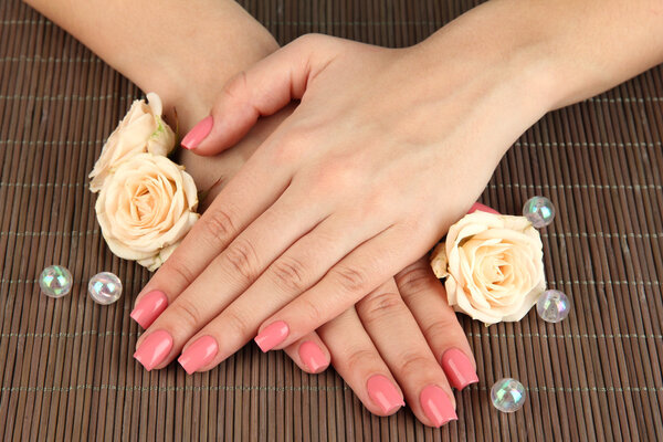 Woman hands with pink manicure and flowers, on bamboo mat background