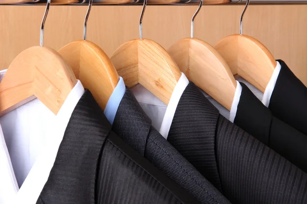 Suits with shirts on hangers on wooden background — Stock Photo, Image