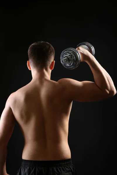 Handsome young muscular sportsman execute exercise with dumbbell on dark background — Stock Photo, Image