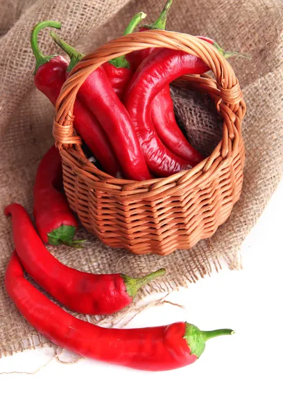 Red hot chili peppers in wicker basket,on sackcloth, isolated on white — Stock Photo, Image