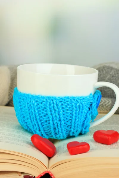 Cup with knitted thing on it and open book close up — Stock Photo, Image