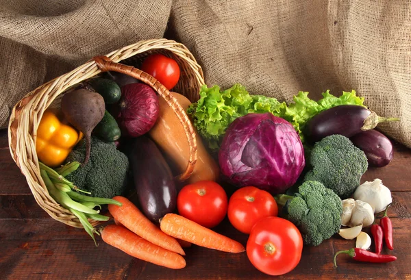 Diferentes verduras en cesta en la mesa sobre fondo de saco —  Fotos de Stock
