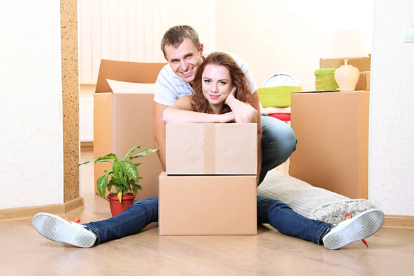 Young couple with boxes in new home on room background — Stock Photo, Image