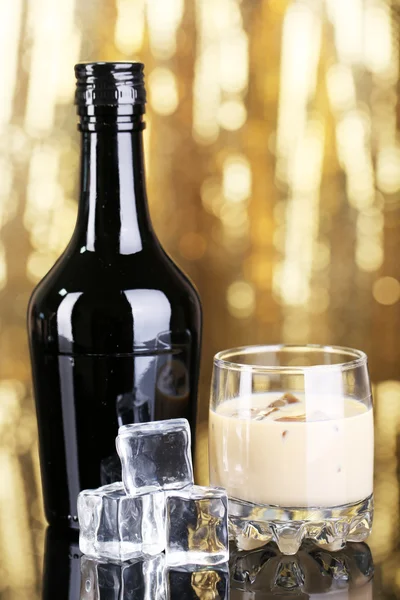 Liqueur Baileys en bouteille et verre sur fond doré — Photo