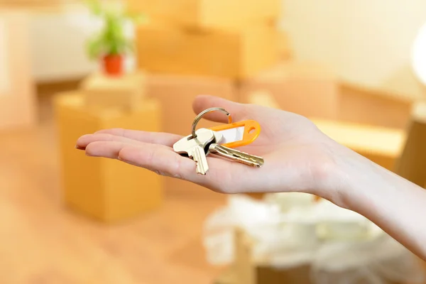 Female hand with keys ob stack of cartons background: moving house concept — Stock Photo, Image
