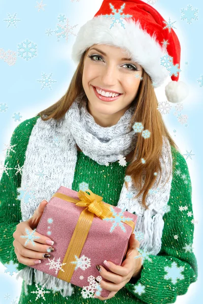 Beautiful smiling girl in New Year hat with gift on blue background — Stock Photo, Image