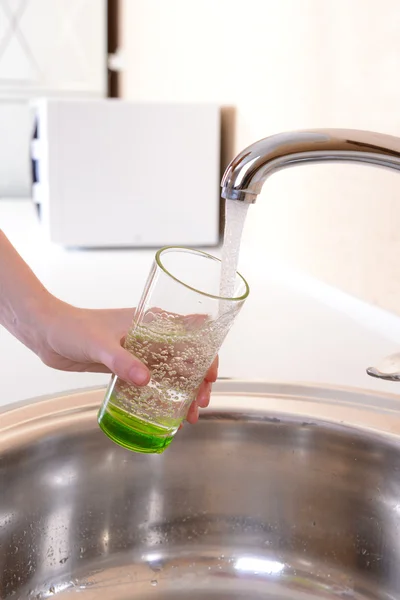 Mão segurando vidro de água derramada da torneira da cozinha — Fotografia de Stock