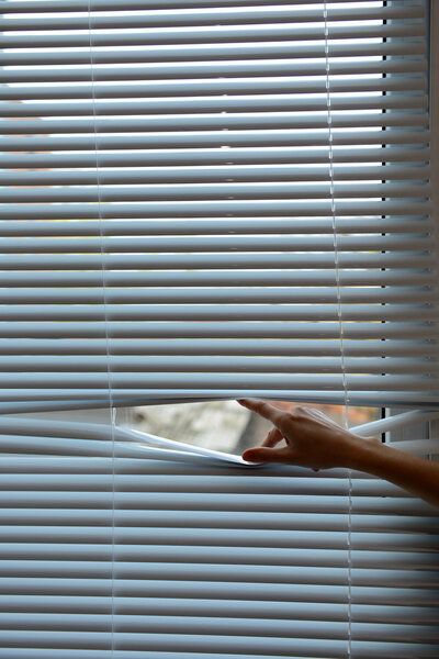 Female hand separating slats of venetian blinds with a finger to see through