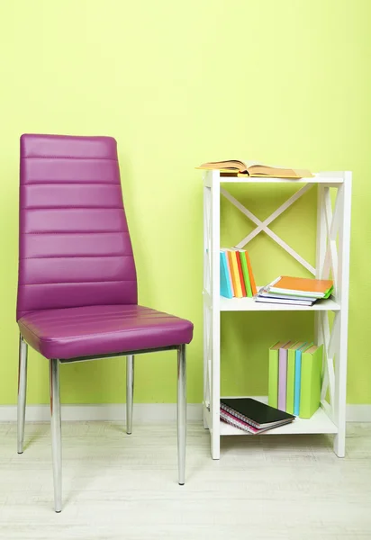 Beautiful interior with modern color chair, books on wooden stand, on wall background — Stock Photo, Image