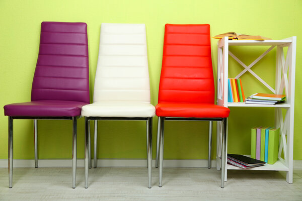 Beautiful interior with modern color chairs, books on wooden stand, on wall background