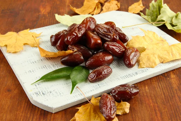 Dates sèches avec feuilles jaunes sur fond en bois — Photo