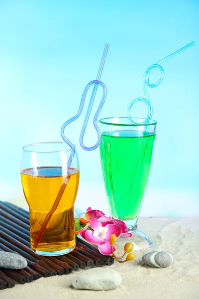 Glasses of cocktails on sand, on bright background — Stock Photo, Image