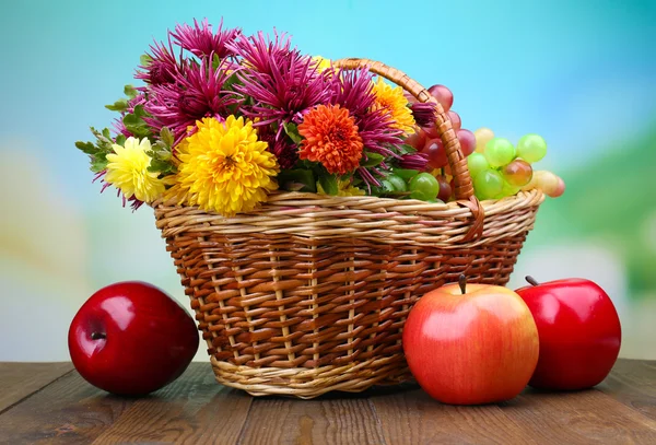 用美丽的鲜花在柳条编织的篮子和水果，在明亮的背景上的组成 — 图库照片
