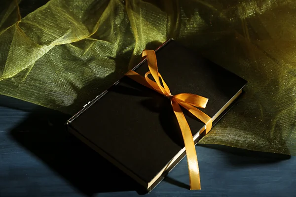 Книга, обгорнута кольоровою стрічкою, на дерев'яному фоні — стокове фото