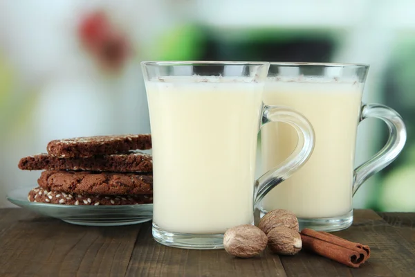 Cups of eggnog with cinnamon and cookies on table on bright background — Stock Photo, Image