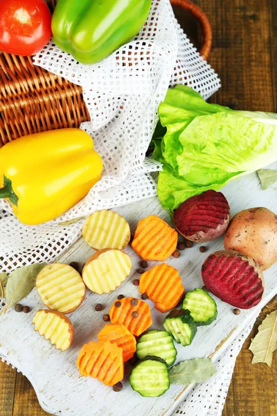 Beautiful sliced vegetables, on wooden board, on wooden background — Stock Photo, Image