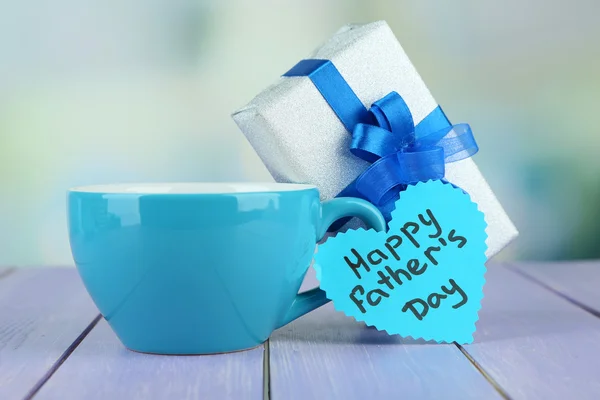 Happy Fathers Day tag with gift box and cup, on wooden table, on light background — Stock Photo, Image