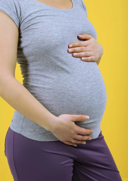 Zwangere vrouw aanraken haar buik op gele achtergrond — Stockfoto
