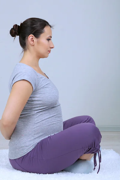 Mujer embarazada joven haciendo ejercicios sobre alfombra en el fondo de la pared — Foto de Stock