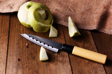 Mutfak bıçağı ve yeşil elma, ahşap arka planda.