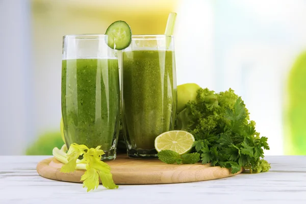 Glasses of green vegetable juice on wooden table on bright background — Stock Photo, Image