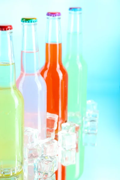 Getränke in Glasflaschen mit Eiswürfeln auf blauem Hintergrund — Stockfoto