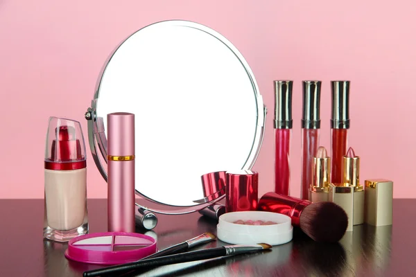 Round table mirror with cosmetics on table on pink background