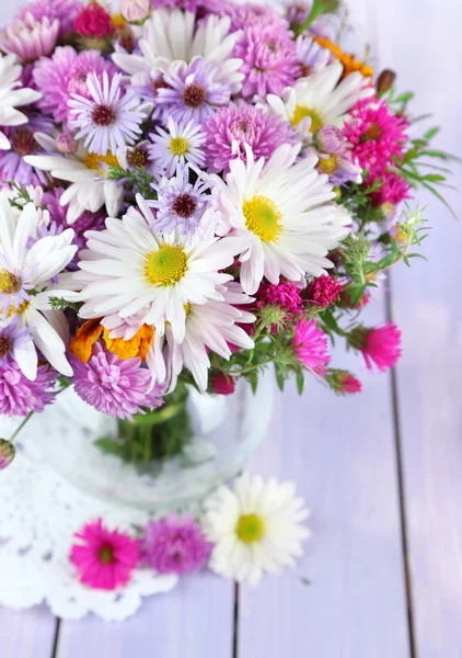 Wildflowers in glass vase on napkin on wooden table — Stock Photo, Image